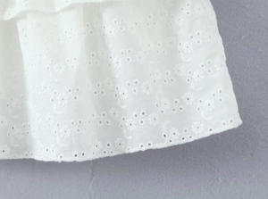 Detailaufnahme des weißen ärmellosen Minikleids mit aufwendiger floraler Lochstickerei-Struktur