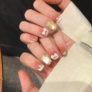 Detail of pink ombré press-on nails with 3D bows, gold foil, and floral patterns