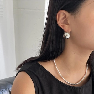 Close-up of minimalist silver wide hoop earrings and matching bead necklace on model