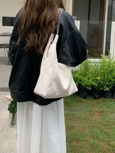 Outdoor shot of cream-white chain tote bag worn with a black leather jacket