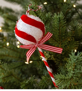 Detail of red and white glittery candy cane ornament hanging on a lit Christmas tree