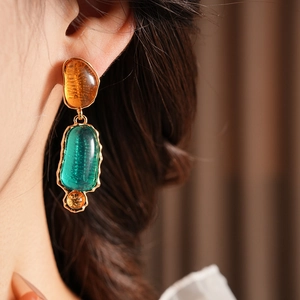 Close-up of vintage resin earrings featuring amber and green stones with gold trim