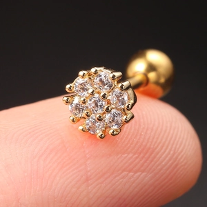 Close-up of a tiny golden flower earring with clear cubic zirconia held on a fingertip