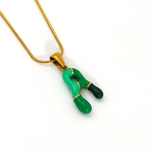 Collana in acciaio dorato con ciondolo a lettera in smalto verde su sfondo bianco
