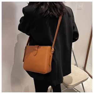 Detailed view of a brown vintage leather shoulder bag with buckle on a model in a black suit
