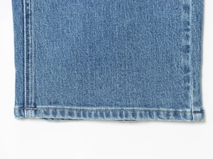 Detailed close-up of dark blue washed denim hem with reinforced stitching and twill texture