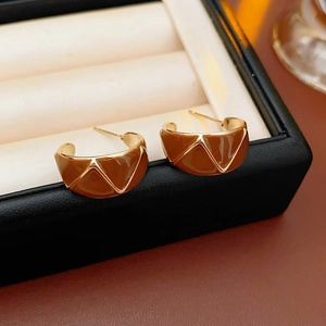 Macro shot of brown enamel C-shape earrings with gold geometric lines on a jewelry tray
