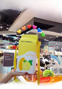 Detail of yellow lemon juice box crossbody bag with strap in hand against grocery background