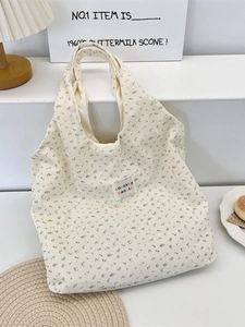 Off-white corduroy tote bag with blue floral patterns and shoulder straps on a white stand