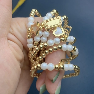 Close-up of layered pearl and gold bead bracelets with heart and star charms