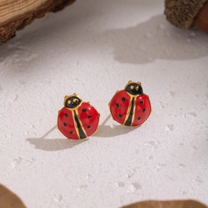 Gros plan de boucles d'oreilles coccinelle rouge et noir avec détails dorés sur pierre
