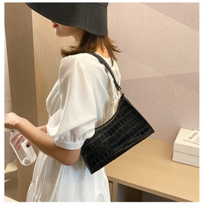 Detail view of black crocodile pattern baguette bag worn as a shoulder underarm bag