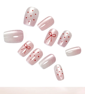 Macro detail of pink cat-eye press-on nails with red bow designs and polka dots