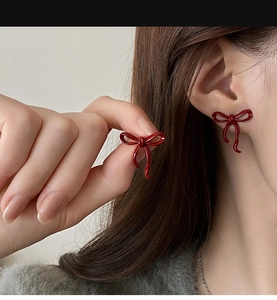 Close-up of red enamel bow earrings on a model to show texture and delicate metal finish