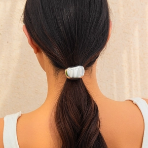 Close-up of a glossy silver irregular pebble metal hair tie on a white ponytail