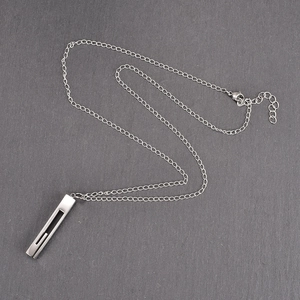 Detail view of silver geometric bar pendant with hollow slot on textured stone background