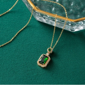Close-up of emerald-cut green pendant with gold chain on luxury dark textured background