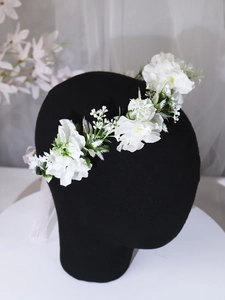 Detail of white artificial flower headband with fabric petals and delicate green leaves