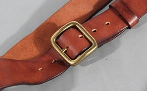 Detailed close-up of brown genuine leather belt texture and brass pin buckle hardware
