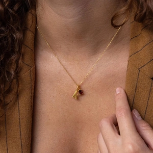 Gold necklace featuring letter K pendant with a rectangular red gemstone on a model