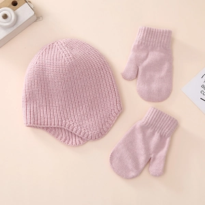 Detailed flat lay of soft pink knitted baby hat and matching mittens set on warm background