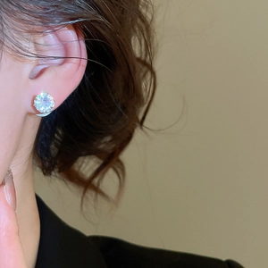 Close-up of a silver stud earring with a round sparkling gemstone worn on a model ear