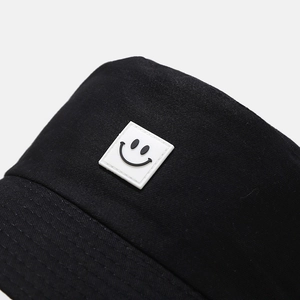 Close-up of black canvas bucket hat featuring a white square PVC smiley face patch detail