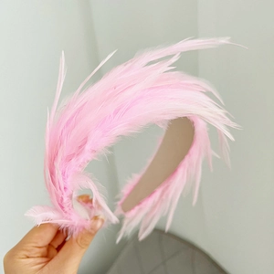 Close-up of a stylish pink feather headband held by hand with natural lighting
