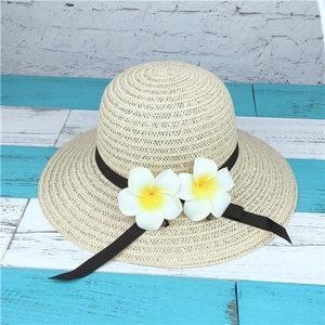 Detail of summer straw hat with black ribbon and tropical frangipani flower accents
