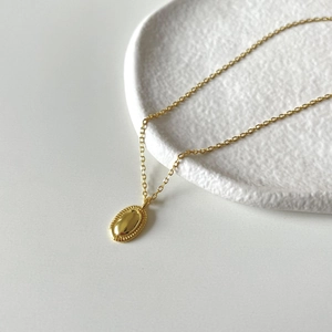 Minimalist gold oval pendant necklace with wheat-ear texture on a white ceramic plate