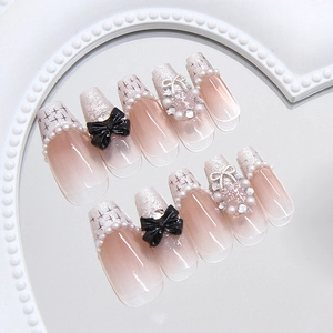 Unghie finte rosa nude stile francese con fiocco nero e dettagli di perle raffinati