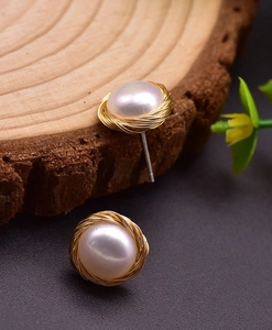 Detail of round pearl stud earrings featuring a golden woven wire bird nest frame