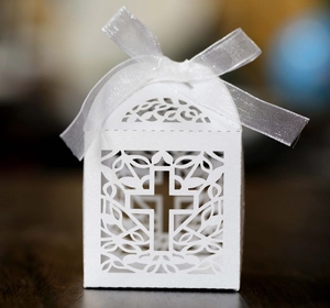 Close-up of white laser-cut wedding favor box with cross design and satin ribbon bow