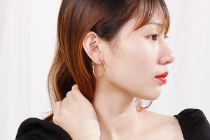 Close-up of a model wearing large rose gold hoop earrings in polished titanium steel