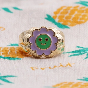 Detailed macro shot of a gold-plated flower ring with purple petals and green smiley face