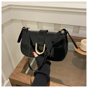 Close-up of a black glossy patent leather shoulder bag with a gold U-shaped metal buckle