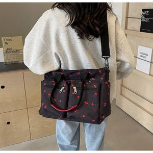 Detail of a large black nylon tote bag with red cherry print worn by a model