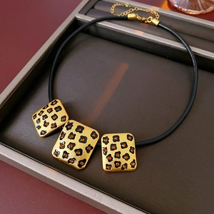 Detail of square gold pendant with leopard print and orange crystals on black cord