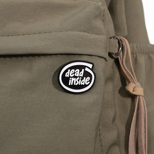 Détail du sac à dos en toile vert olive avec un badge circulaire texte 'dead inside'