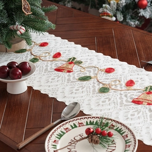 Christmas lace table runner with embroidered bells and tassels on wooden table