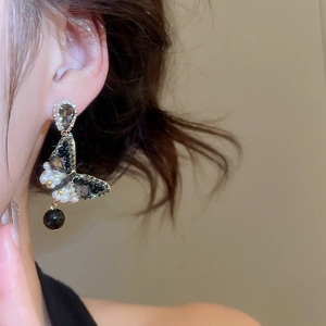 Detail of silver needle earrings featuring black butterfly motif with zircon and pearls