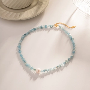 Detail of light blue stone fragments and white pearl necklace with gold-plated chain