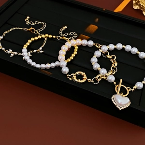 Dettaglio del set di braccialetti dorati a più strati con perle e cuore
