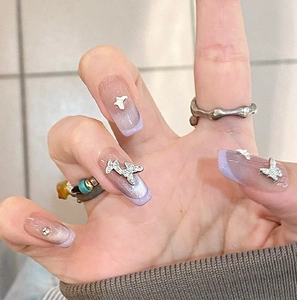 Detail of purple cat-eye press-on nails with 3D silver butterflies and French tips