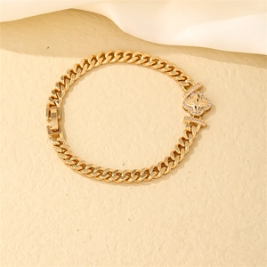 Detail shot of golden Cuban link bracelet with clover zircon inlay on white silk
