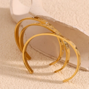 Close-up of three 18K gold plated C-shape bangles with sea patterns and small gemstones
