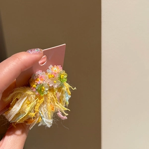 Detailed view of handmade floral stud earrings with vibrant yellow fringe tassels and beads