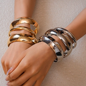 Detailed view of polished gold and silver chunky cuff bracelets on a model wrist