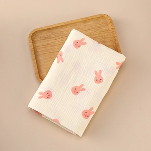 Detail of soft beige muslin swaddle with pink rabbit patterns on a wooden tray