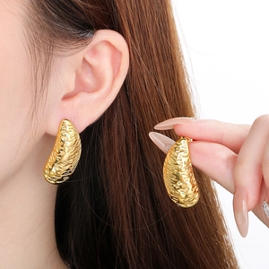 Detailed close-up of irregular textured gold earrings worn to show style and size